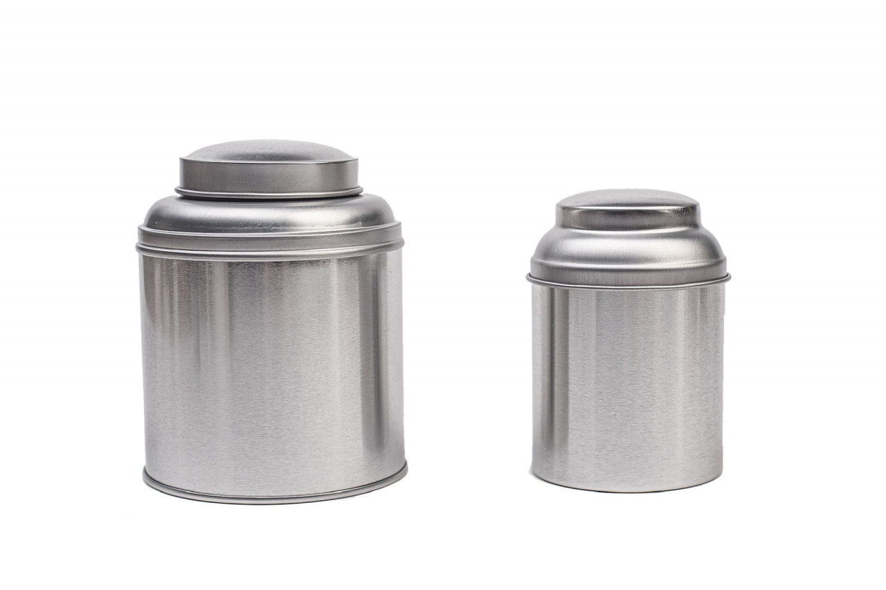 Zwei geschlossene silberfarbene Teedosen aus Metall mit Aromadeckel, eine größere und eine kleinere Dose nebeneinander auf weißem Hintergrund.