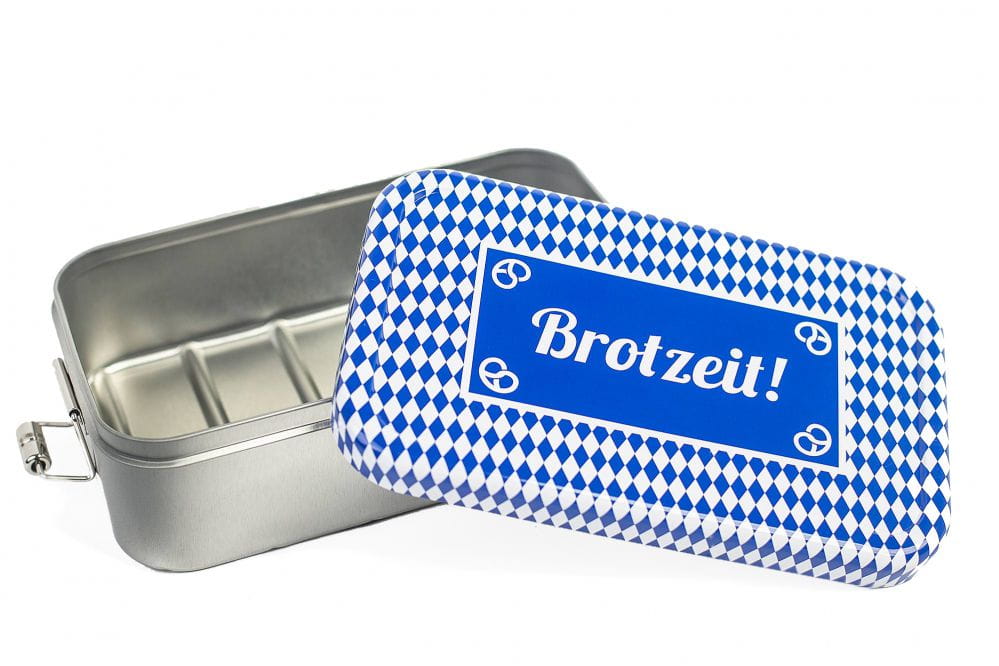 Geöffnete eckige Lunchbox aus silberfarbenem Metall mit abgenommenem Deckel im blau-weißen Rautenmuster und der Aufschrift „Brotzeit!“, innen mit Fächereinteilung, auf weißem Hintergrund.