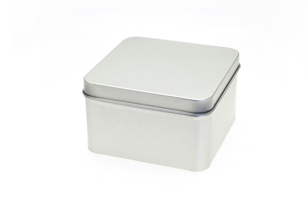 Geschlossene quadratische Blechdose aus silberfarbenem Metall mit aufgesetztem Stülpdeckel, auf weißem Hintergrund fotografiert.